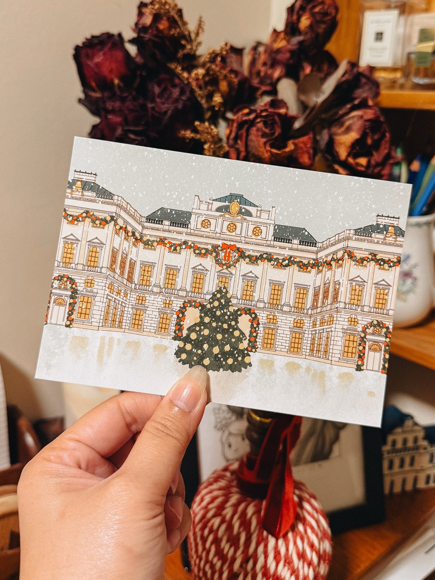 Clarence House holiday illustration card held in front of a desk